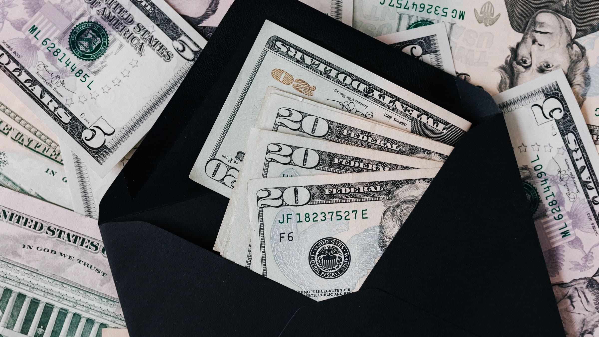Twenty-dollar bills tucked inside a black envelope lying on a spread of other banknotes