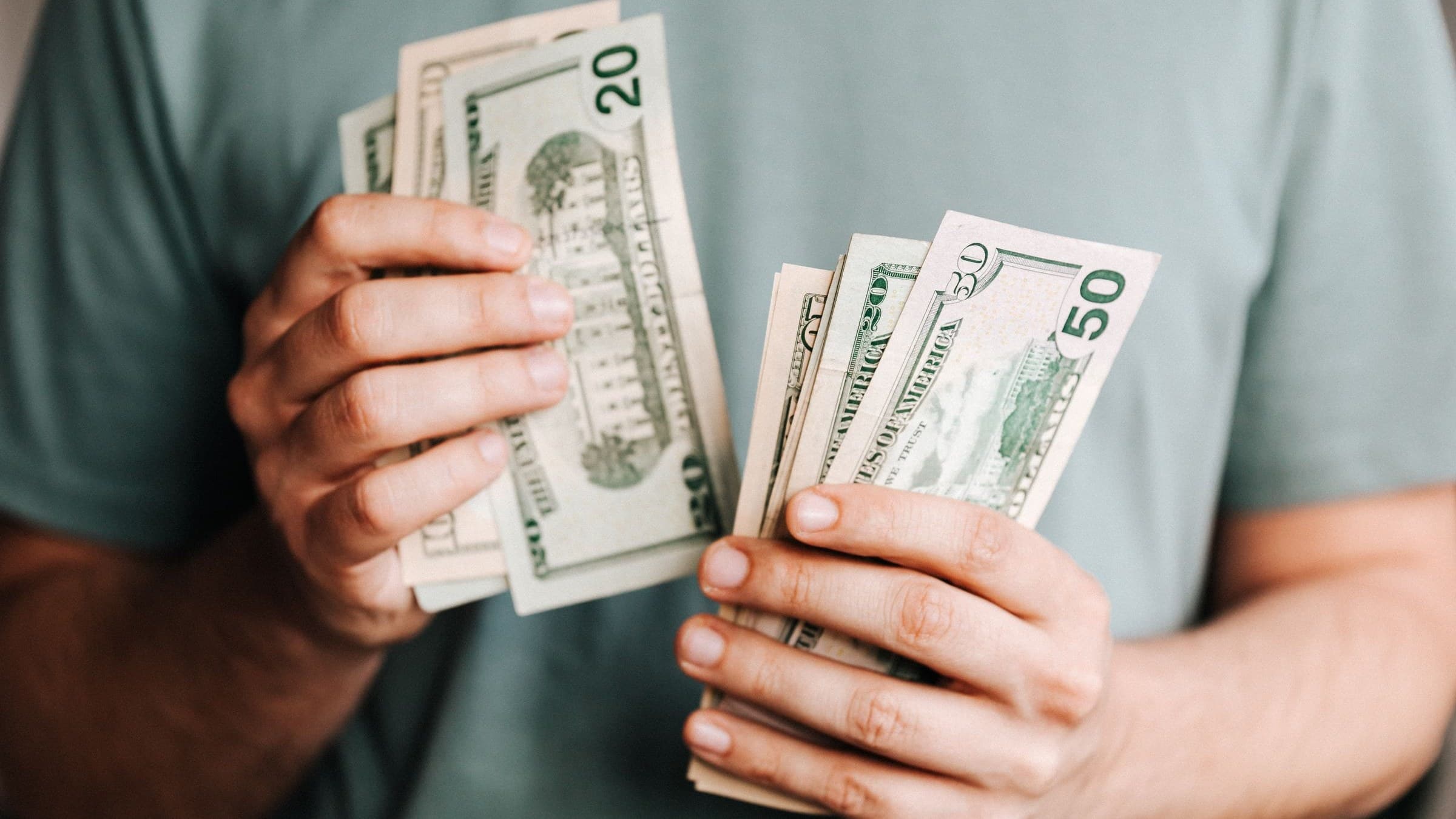 Close-up of two hands counting twenty and fifty-dollar bills against a grey t-shirt